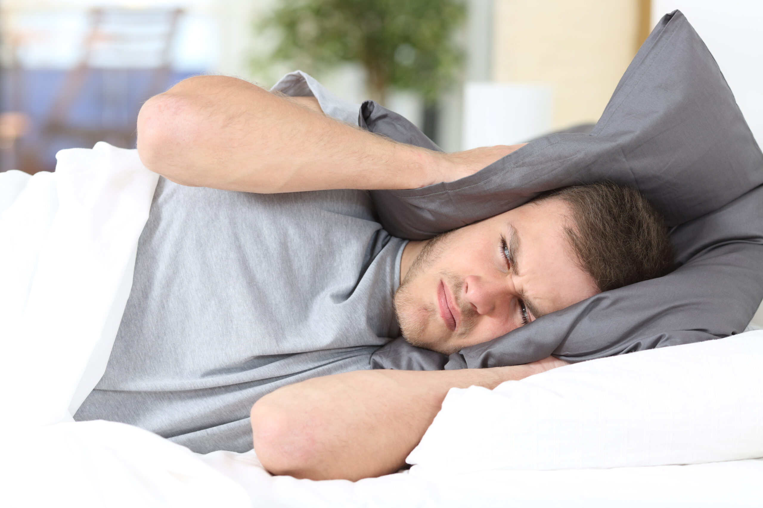One,man,trying,to,sleep,covering,ears,to,avoid,neighbor